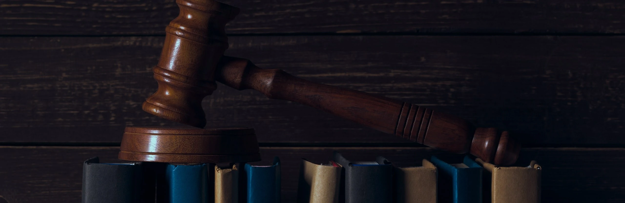 Wooden gavel rests atop stacked law books against a dark wooden Wooden gavel rests atop stacked law books against a dark wooden